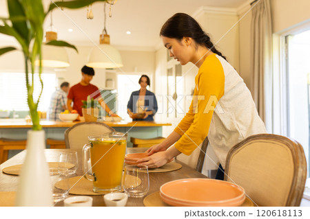Setting table with plates and glasses, young asian woman preparing family meal in kitchen Setting table with plates and glasses, young asian woman preparing family meal in kitchen 120618113