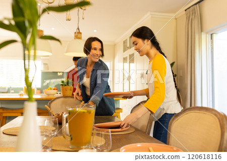 Setting table, mother and daughter preparing for family meal in dining room 120618116