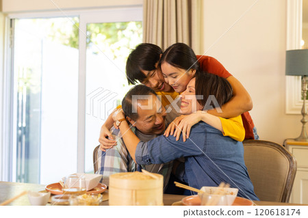At home, asian family hugging and smiling around dining table, enjoying quality time together 120618174