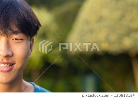 Smiling teenage asian boy with braces outdoors, enjoying nature in garden, copy space 120618184