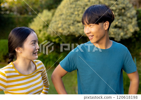 Smiling young asian brother and sister talking and enjoying time together outdoors in garden 120618198