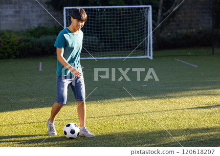 Playing soccer, teenage asian boy dribbling ball on grass field in backyard, outdoors, copy space Playing soccer, teenage asian boy dribbling ball on grass field in backyard, outdoors, copy space 120618207