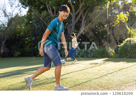 Playing soccer outdoors, smiling asian boy enjoying time with family in park Playing soccer outdoors, smiling asian boy enjoying time with family in park 120618209