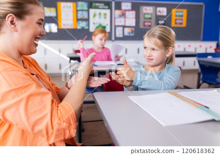Practicing sign language, female teacher and student in school classroom, smiling together 120618362
