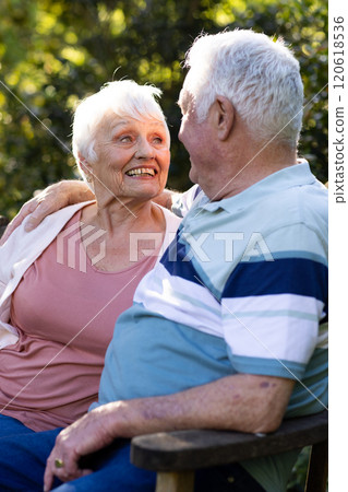 Happy caucasian senior couple sitting on bench, embracing and smiling in sunny garden, copy space Happy caucasian senior couple sitting on bench, embracing and smiling in sunny garden, copy space 120618536