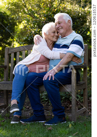 Happy caucasian senior couple sitting on bench and embracing in sunny garden, copy space Happy caucasian senior couple sitting on bench and embracing in sunny garden, copy space 120618537