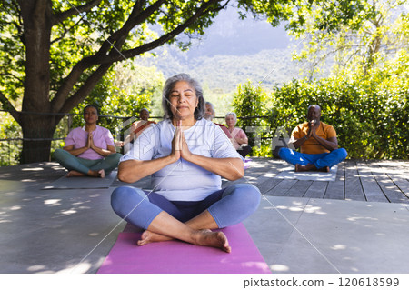 Focused biracial senior woman practising yoga with friends in sunny garden, copy space Focused biracial senior woman practising yoga with friends in sunny garden, copy space 120618599