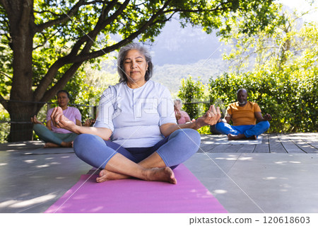 Focused biracial senior woman practising yoga with friends in sunny garden, copy space 120618603