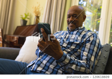 Smiling elderly African American man on sofa, using smartphone in sunny room Smiling elderly African American man on sofa, using smartphone in sunny room 120618609
