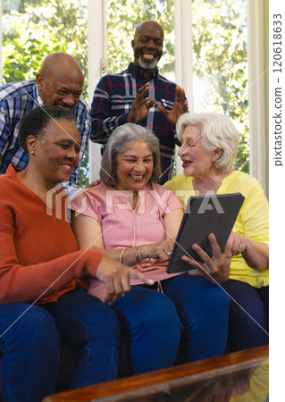 Happy diverse group of senior friends having video call and laughing in sunny living room Happy diverse group of senior friends having video call and laughing in sunny living room 120618633