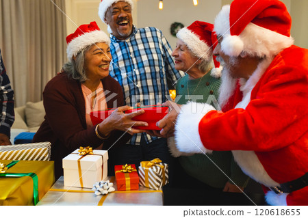 Happy biracial man in santa clothes giving gifts to friends in living room at home Happy biracial man in santa clothes giving gifts to friends in living room at home 120618655