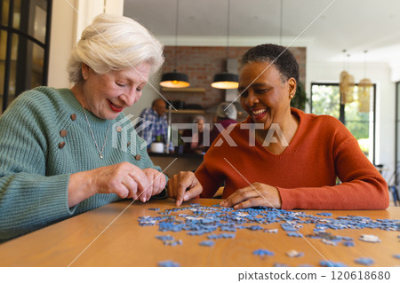 Happy diverse senior female friends playing with jigsaw puzzles in sunny dining room at home 120618680