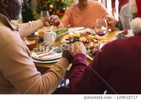 Hands of diverse group of senior friends saying grace at christmas dinner in sunny dining room 120618717