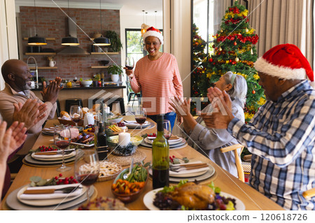 Happy african american senior woman in santa hat toasting at christmas dinner in sunny dining room 120618726
