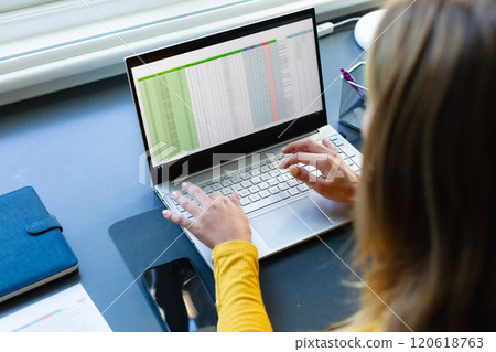 Caucasian woman sitting at desk, working from home and using laptop in sunny room 120618763