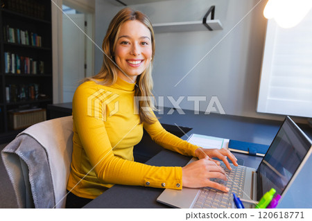 Caucasian woman sitting at desk, working from home, using laptop and smiling in sunny room Caucasian woman sitting at desk, working from home, using laptop and smiling in sunny room 120618771