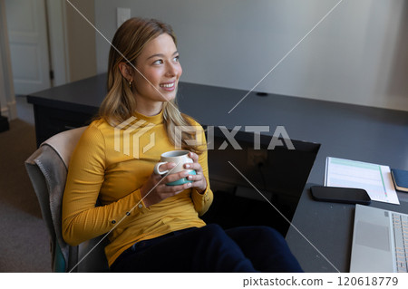 Caucasian woman sitting at desk, working from home with laptop and drinking coffee in sunny room Caucasian woman sitting at desk, working from home with laptop and drinking coffee in sunny room 120618779