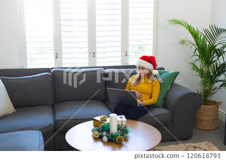 Happy caucasian woman in santa hat using laptop and smiling at christmas at home Happy caucasian woman in santa hat using laptop and smiling at christmas at home 120618793