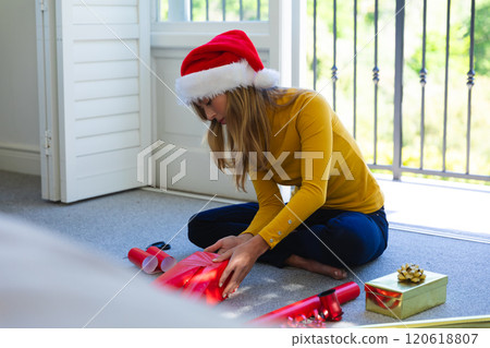 Happy caucasian woman in santa hat sitting on floor and packing gifts at christmas at home Happy caucasian woman in santa hat sitting on floor and packing gifts at christmas at home 120618807