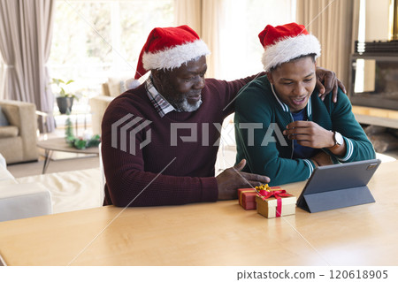 Happy african american father and son in christmas hats having tablet video call at home 120618905