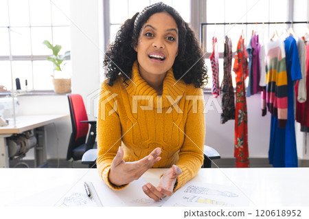 Happy biracial female fashion designer having video call at desk in studio 120618952