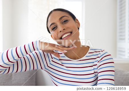 Portrait of happy biracial woman with striped blouse sitting on couch at home 120618959