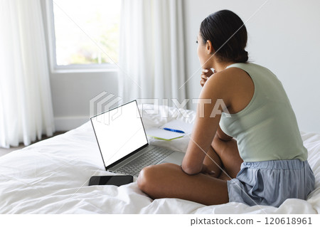 Busy biracial woman with smartphone and notebook using laptop with copy space in bedroom Busy biracial woman with smartphone and notebook using laptop with copy space in bedroom 120618961