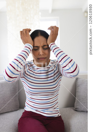 Biracial woman sitting on couch and touching her head at home 120618980