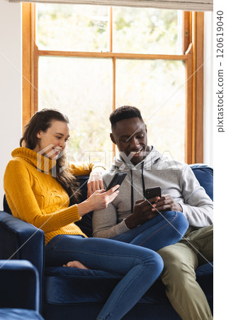 Happy diverse couple sitting on sofa using smartphones at home 120619040