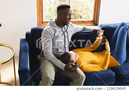 Happy diverse couple sitting on sofa using smartphones at home 120619045