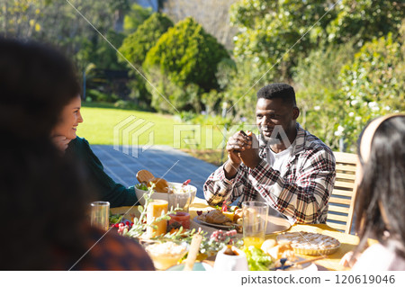 Happy diverse male and female friends eating thanksgiving celebration meal in sunny garden 120619046