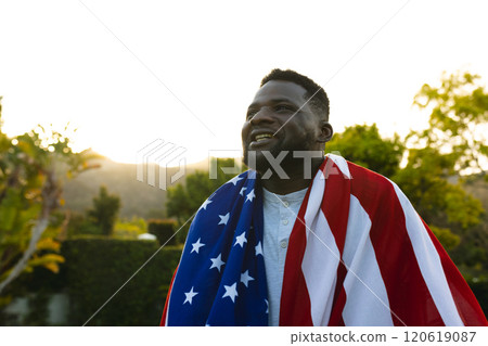 Happy african american man with flag on back american flag in sunny garden Happy african american man with flag on back american flag in sunny garden 120619087