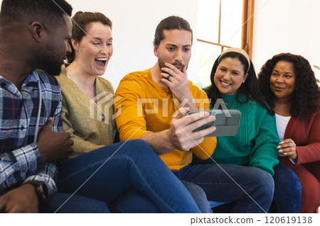 Happy diverse male and female friends relaxing at home together talking and looking at smartphone 120619138