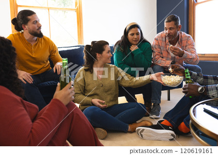 Happy diverse male and female friends talking, eating popcorn and drinking beer at home Happy diverse male and female friends talking, eating popcorn and drinking beer at home 120619161