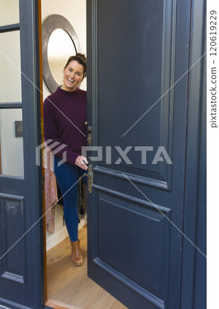Happy caucasian woman in sweater standing in doorway and laughing on sunny day 120619229