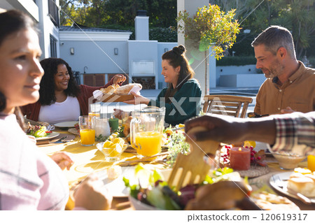 Happy diverse male and female friends eating thanksgiving celebration meal in sunny garden 120619317