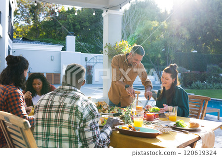 Happy diverse male and female friends eating thanksgiving celebration meal in sunny garden 120619324