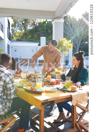 Happy diverse male and female friends eating thanksgiving celebration meal in sunny garden 120619326