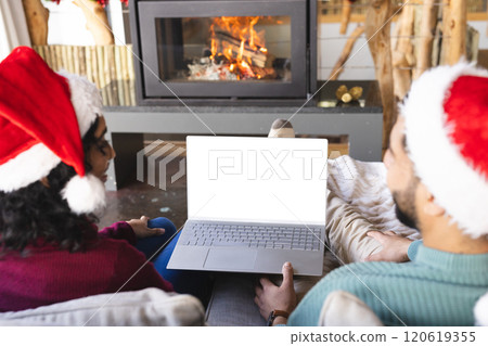 Biracial couple with santa hats having video call on laptop at christmas at home, copy space Biracial couple with santa hats having video call on laptop at christmas at home, copy space 120619355