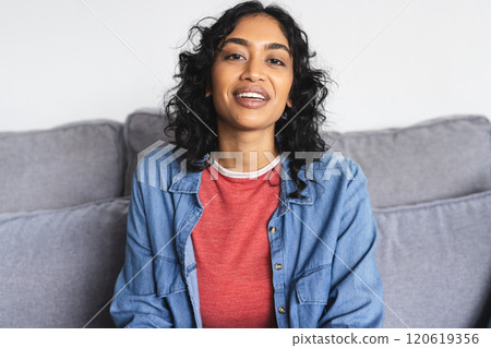 Happy biracial woman sitting on sofa and having video call in living room at home Happy biracial woman sitting on sofa and having video call in living room at home 120619356