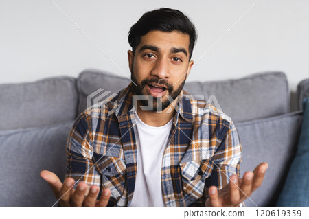 Happy biracial man sitting on sofa, having video call and gesticulating in living room at home Happy biracial man sitting on sofa, having video call and gesticulating in living room at home 120619359