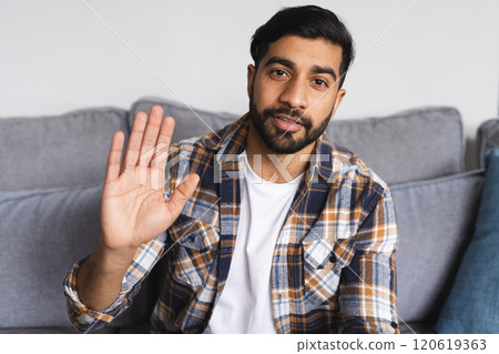 Happy biracial man sitting on sofa, having video call and waving hand in living room at home Happy biracial man sitting on sofa, having video call and waving hand in living room at home 120619363
