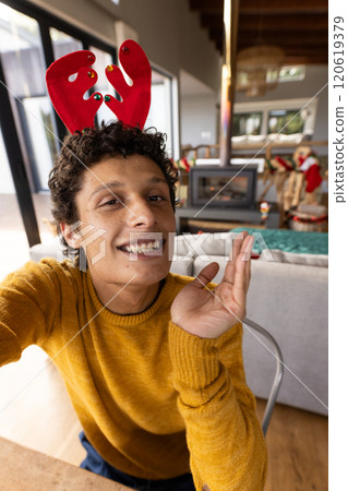 Portrait of happy biracial man wearing reindeer antlers and having video at christmas at home 120619379