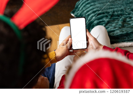 Diverse gay male couple wearing christmas hats and having smartphone video call at home, copy space Diverse gay male couple wearing christmas hats and having smartphone video call at home, copy space 120619387
