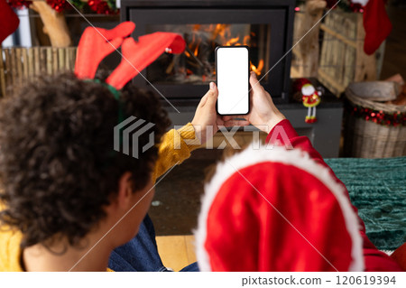 Diverse gay male couple wearing christmas hats and having smartphone video call at home, copy space 120619394