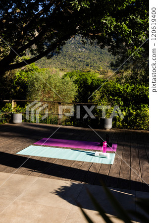 Water bottle, towel and two yoga mats side by side on deck in sunny garden, copy space Water bottle, towel and two yoga mats side by side on deck in sunny garden, copy space 120619400