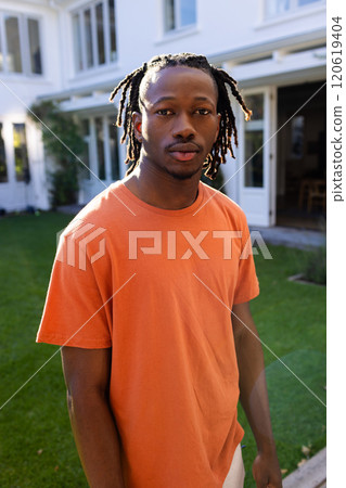 Portrait of african american man with dreadlocks standing outside house in sunny garden 120619404