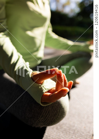Midsection of asian woman practicing yoga meditation sitting in sunny garden 120619416
