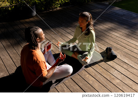 Happy diverse couple practicing yoga meditation sitting facing each other on deck in sunny garden 120619417