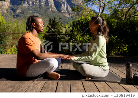 Happy diverse couple practicing yoga meditation sitting holding hands on deck in sunny garden 120619419